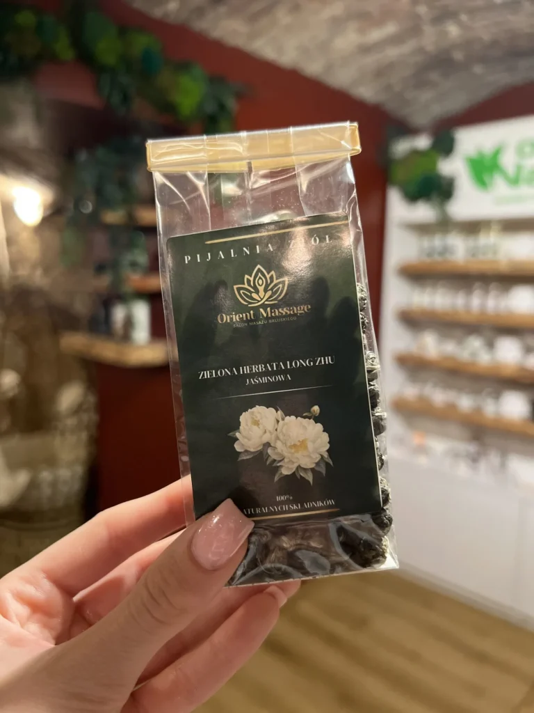 Opakowanie herbaty Orient Massage z rysunkiem białych kwiatów, trzymane w dłoni.