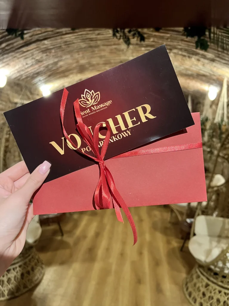 Bordowy voucher podarunkowy i czerwona koperta przewiązane wstążką.
