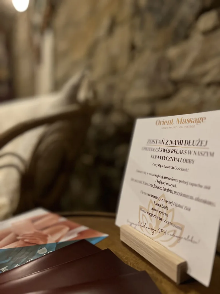 Tabliczka informacyjna i ulotki na stoliku przy kamiennej ścianie.