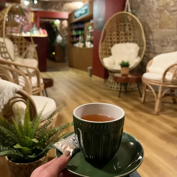 Filiżanka herbaty na zielonym spodku, z rattanowymi fotelami w tle.